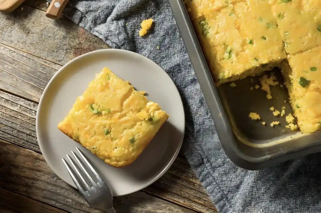 Jiffy Mexican Cornbread Recipe: Easy & Irresistible in 5 Min Slice of cheesy jalapeño cornbread on a plate next to a baking pan of this easy cornbread recipe