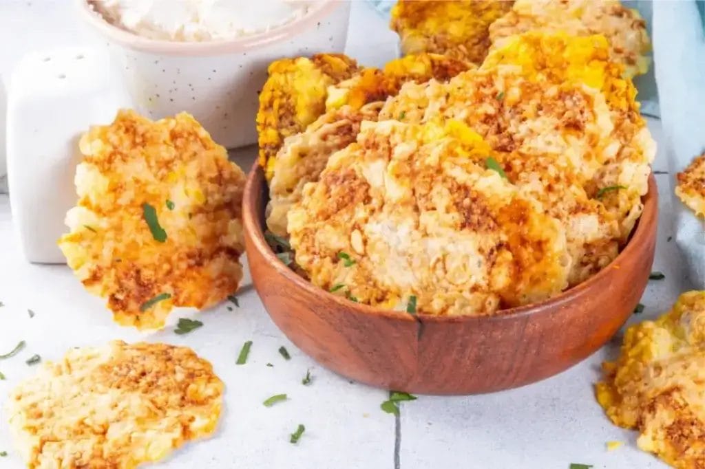 Golden, crispy cottage cheese chips in a wooden bowl, garnished with fresh herbs.